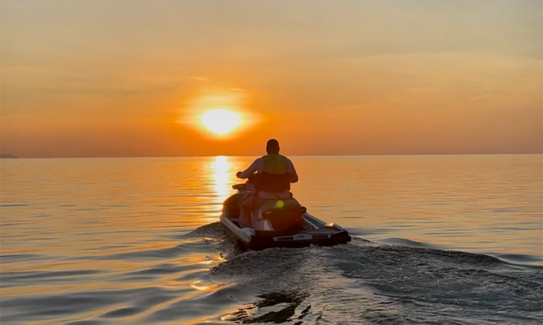 Una moto acuática navega por el mar hacia la puesta de sol.